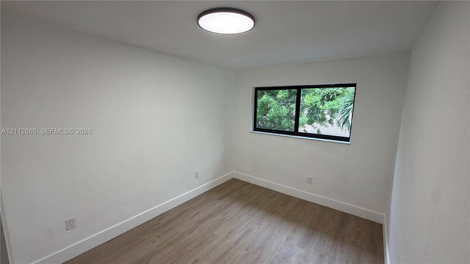 3314 NW 8th, #2, Miami, Miami, FL 33131 Neutral interior space featuring wood-finish flooring, crisp white walls, a flush-mount ceiling light fixture, and a single-pane window with a black frame