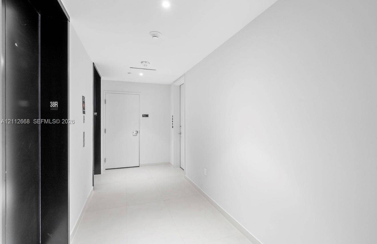 1400 Biscayne Boulevard, #1803, Miami, Miami, FL 33132 Minimalist hallway featuring white tile flooring, high-contrast black elevator doors, and recessed ceiling lighting
