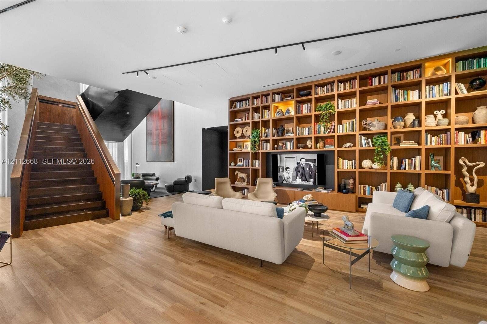 1400 Biscayne Boulevard, #1803, Miami, Miami, FL 33132 Expansive room featuring wood-finish flooring, floor-to-ceiling built-in wooden shelving, a floating-style staircase with wood treads, and recessed track lighting