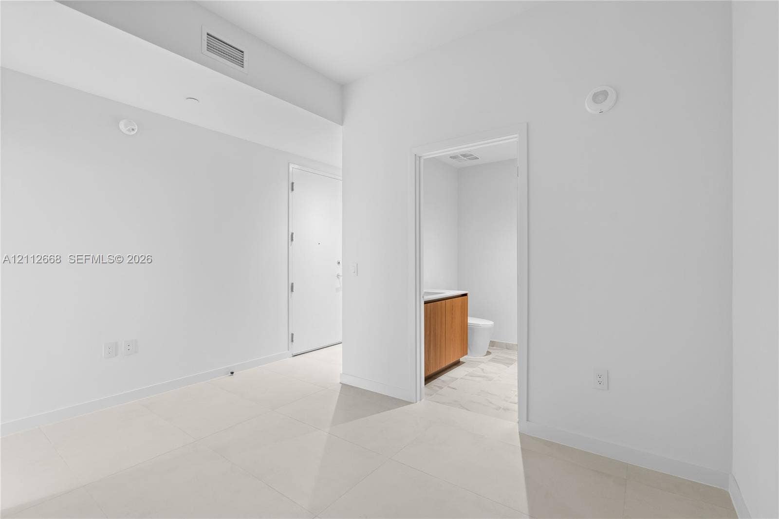 1400 Biscayne Boulevard, #1803, Miami, Miami, FL 33132 Large-format tile flooring, high ceilings, and neutral wall tones, featuring an interior doorway to a bathroom with wood-finish cabinetry and stone-look flooring