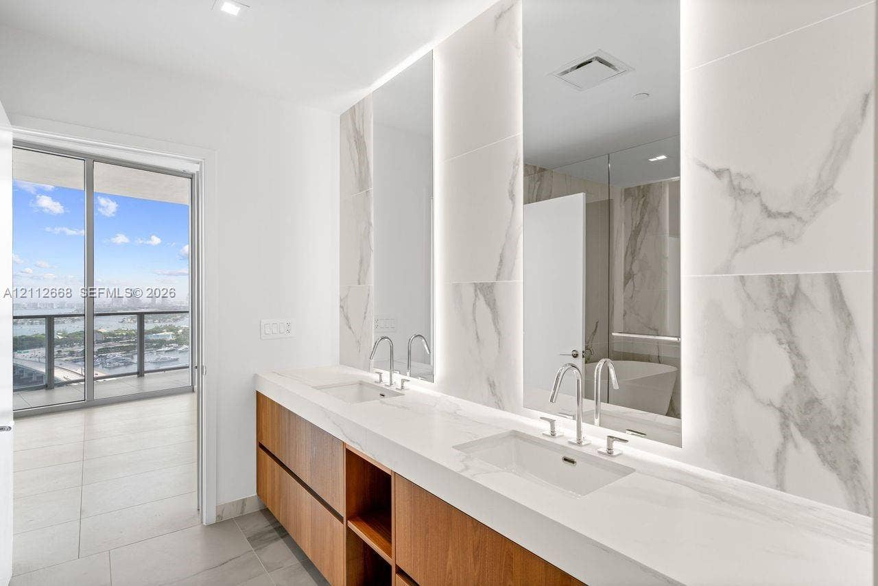 1400 Biscayne Boulevard, #1803, Miami, Miami, FL 33132 Dual-sink vanity with wood-finish cabinetry, stone-surface countertop, floor-to-ceiling stone-tiled backsplash with integrated vertical lighting, and access to a private balcony