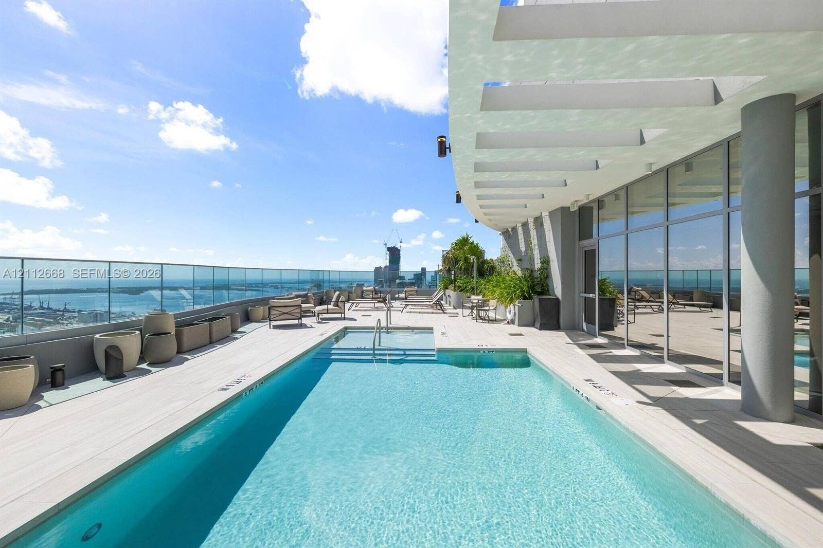 1400 Biscayne Boulevard, #1803, Miami, Miami, FL 33132 Rooftop terrace featuring an in-ground swimming pool, glass paneled perimeter fencing, expansive stone-finish decking, and a structural concrete overhang