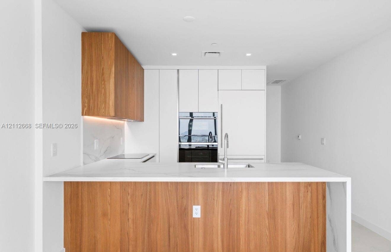 1400 Biscayne Boulevard, #1803, Miami, Miami, FL 33132 Modern kitchen featuring custom wood-finish cabinetry, white flat-panel cabinetry, waterfall-edge stone countertops, integrated appliances, and a stainless steel gooseneck faucet