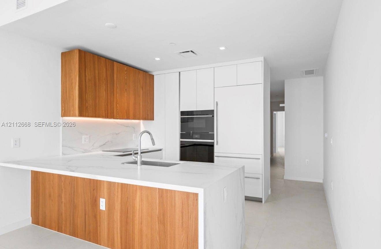 1400 Biscayne Boulevard, #1803, Miami, Miami, FL 33132 Kitchen featuring flat-panel wood-finish cabinetry, white solid surface countertops with integrated backsplash, built-in panel-ready refrigerator, stainless steel undermount sink with arched faucet, and stacked wall oven