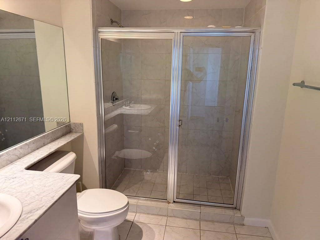 Bathroom featuring a vanity with a stone-top counter, a large wall-mounted mirror, a tiled floor, and a shower enclosure with a glass door and metal trim