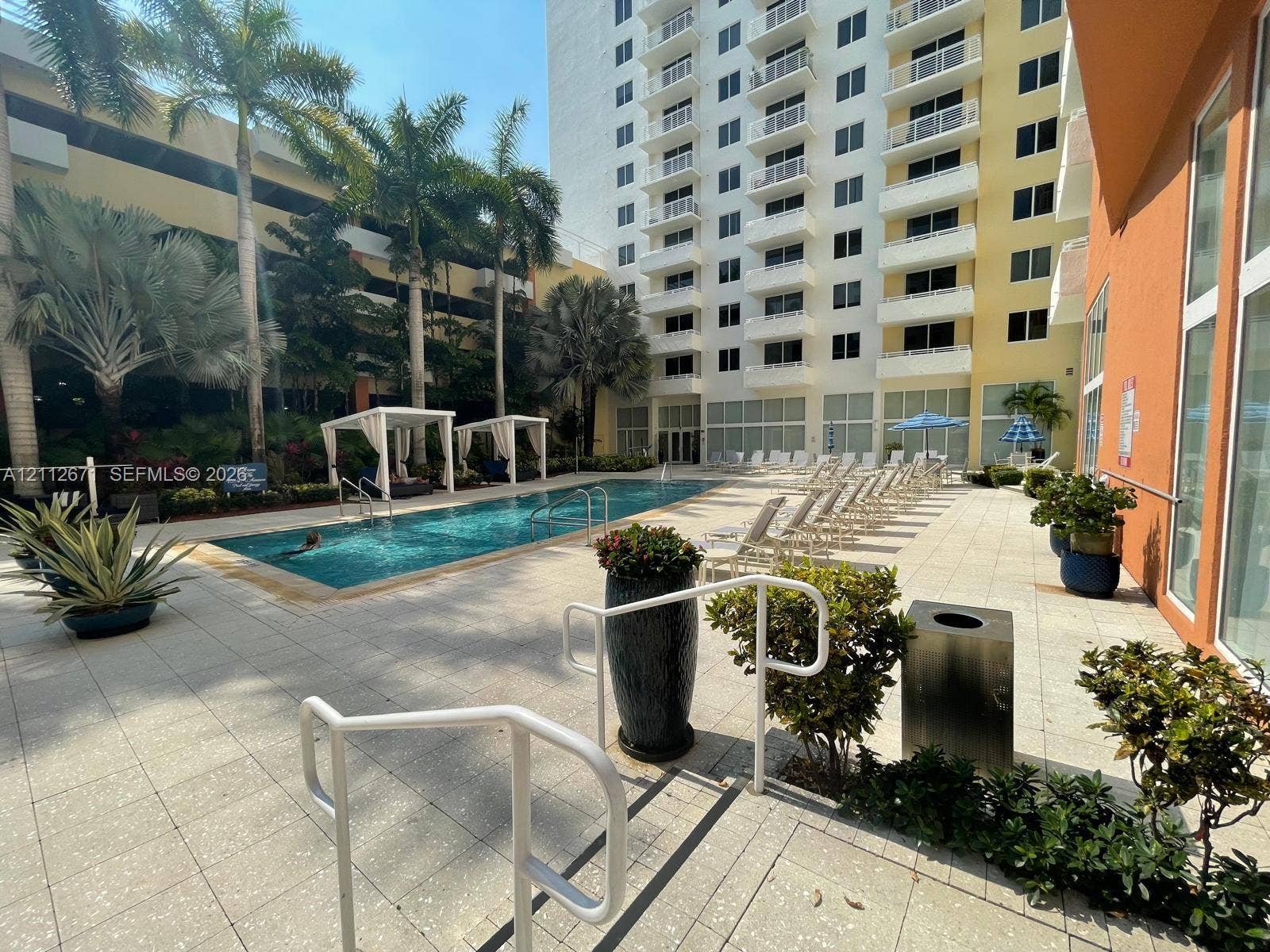 Outdoor swimming pool featuring a paved terrace, cabanas, and mature palm trees