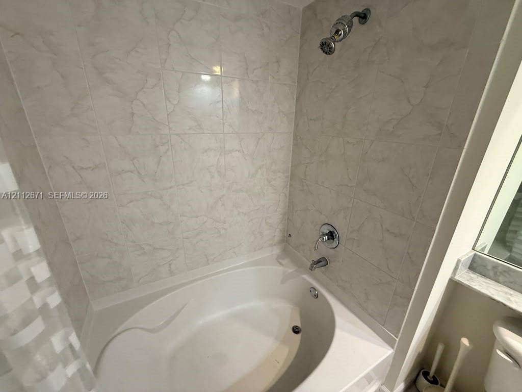 Oval soaking tub featuring light-toned tile surround, polished metal shower fixtures, and integrated ledge shelving