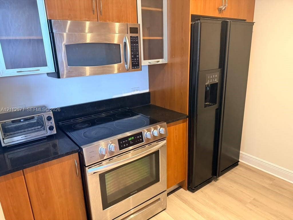 Kitchen featuring wood cabinetry, black solid-surface countertops, stainless steel microwave, stainless steel electric range, and a black refrigerator