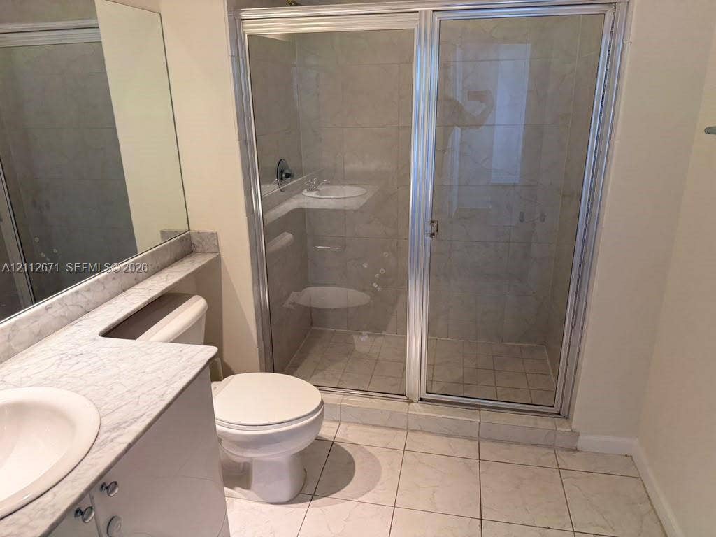 Bathroom featuring a vanity with a patterned stone-finish countertop, undermount sink, large-format tile flooring, and a walk-in shower with a glass enclosure and metal framing