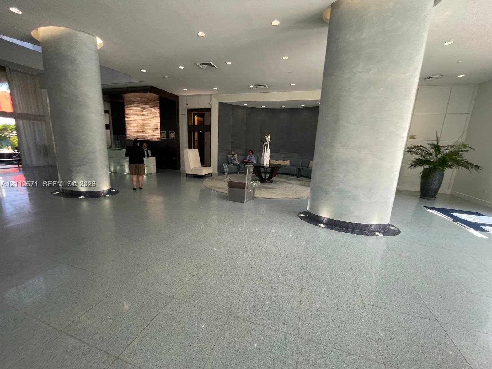 Grand lobby featuring polished stone flooring, dual floor-to-ceiling structural columns, recessed ceiling lighting, and a built-in reception desk