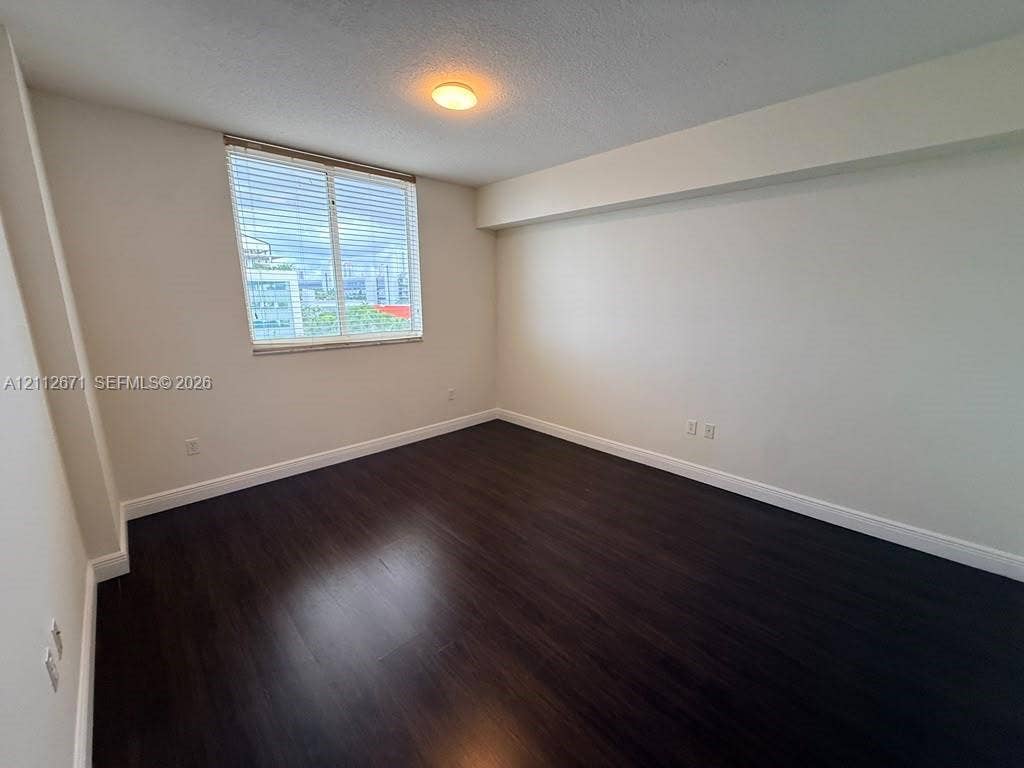 Room featuring dark wood-finish flooring, neutral wall tones, a window with horizontal blinds, and a flush-mount ceiling light fixture