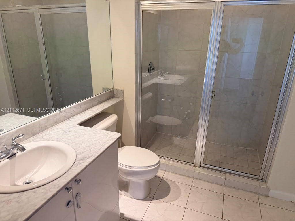 Bathroom featuring a stone-surface vanity with an integrated basin, large wall-mounted mirror, ceramic tile flooring, and a glass-enclosed shower with tiled walls