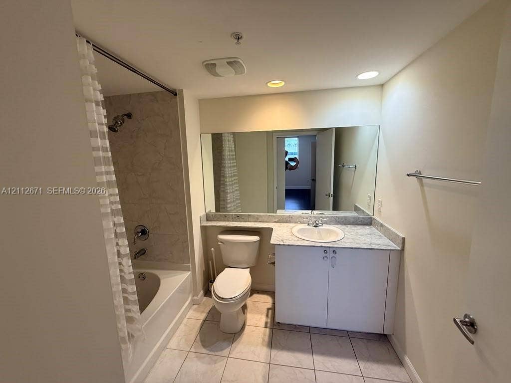 Full-width wall mirror, vanity with stone-surface countertop, integrated basin, tile flooring, and tub-shower combination with tiled surround