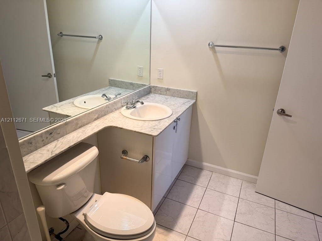 Bathroom featuring a stone-top vanity with an integrated basin, high-gloss cabinetry, full-width wall mirror, and tile flooring