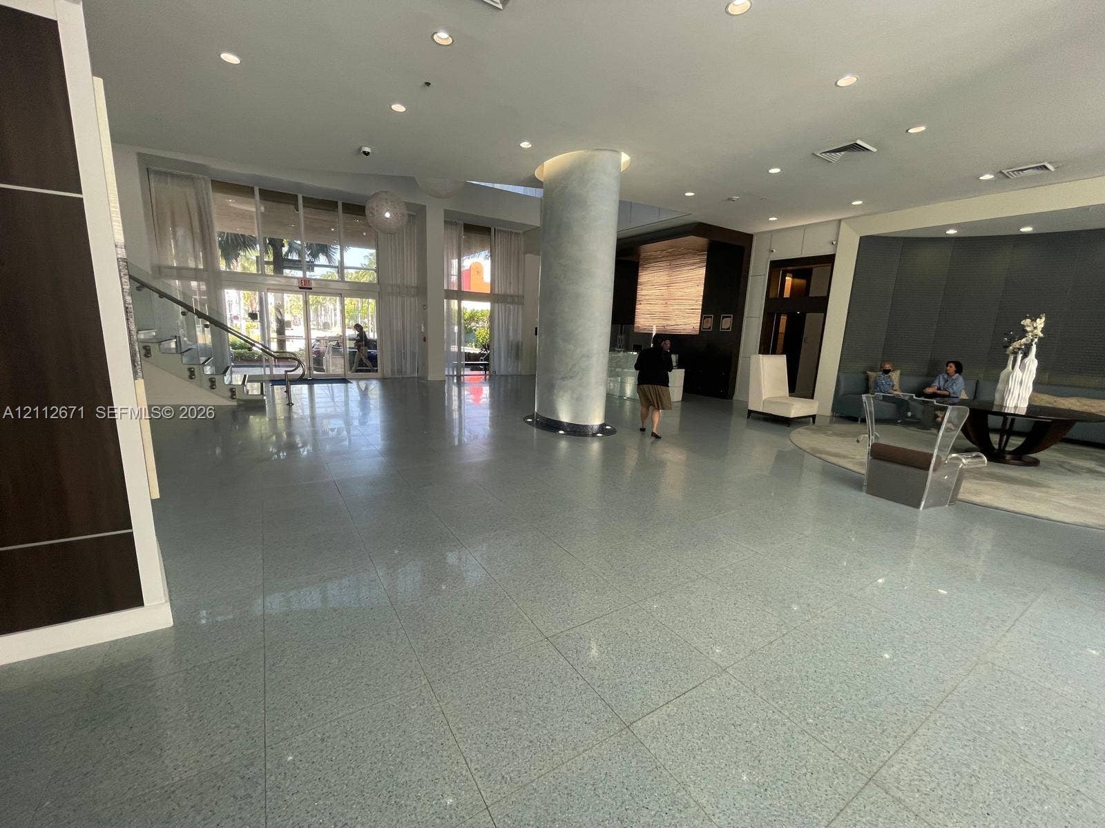 Expansive lobby featuring polished stone flooring, a floor-to-ceiling support column with a high-gloss finish, multi-panel floor-to-ceiling windows, and recessed lighting