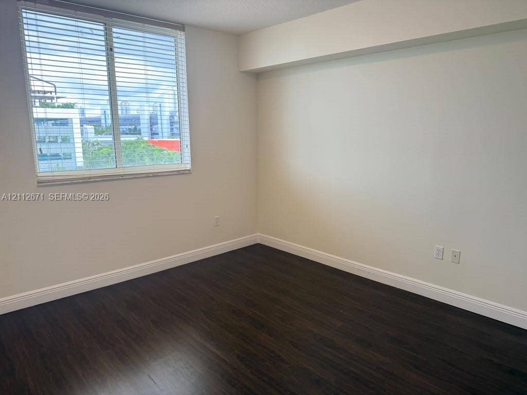 Neutral interior with dark wood-finish flooring, white walls, and a window with horizontal blinds
