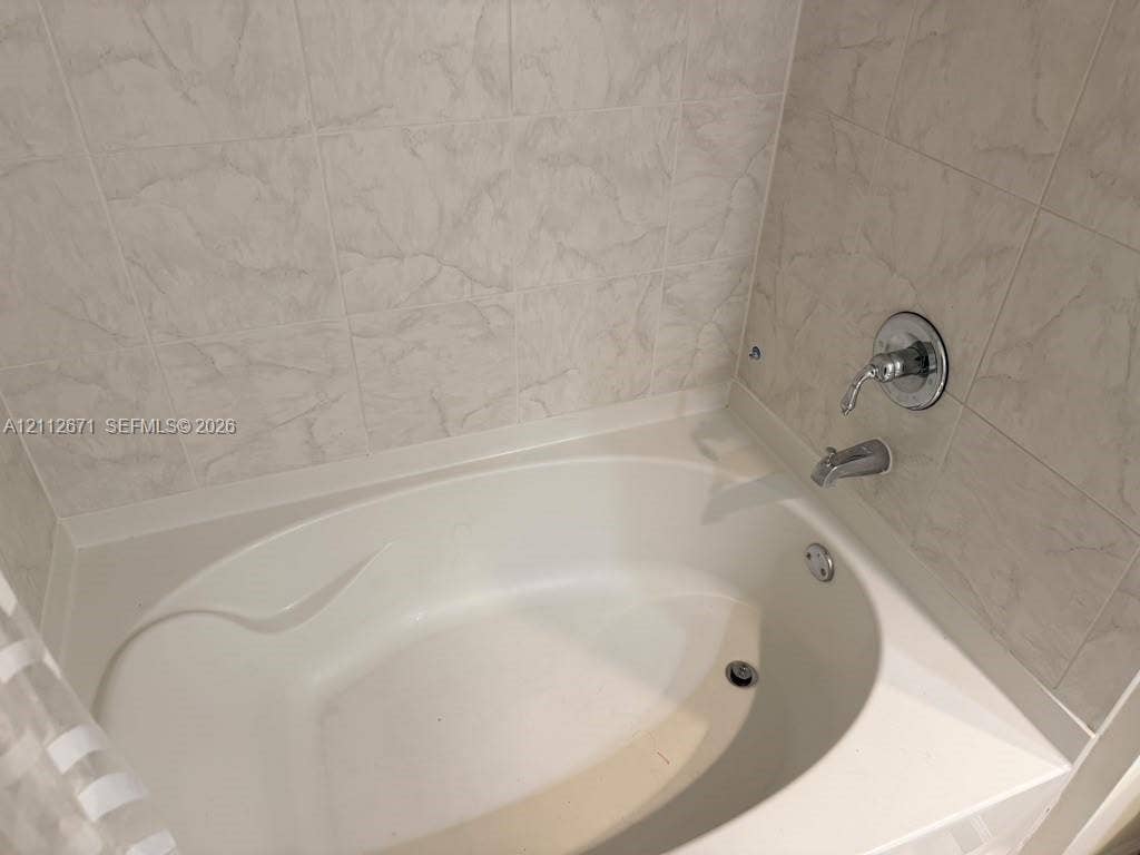 Oval soaking tub featuring light-toned textured tile surround and chrome plumbing fixtures