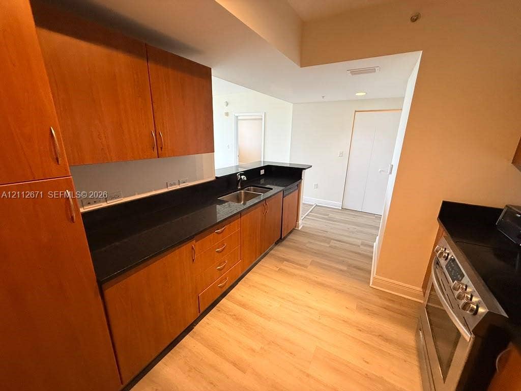 Kitchen featuring wood-finish cabinetry, dark stone countertops, stainless steel appliances, and wood-finish flooring