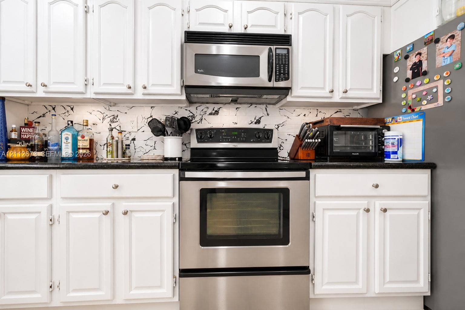 10225 SW 141st Court, #0, Miami, Miami, FL 33186 Kitchen featuring white raised-panel cabinetry, dark solid-surface countertops, patterned tile backsplash, and stainless steel appliances including an over-the-range microwave and range
