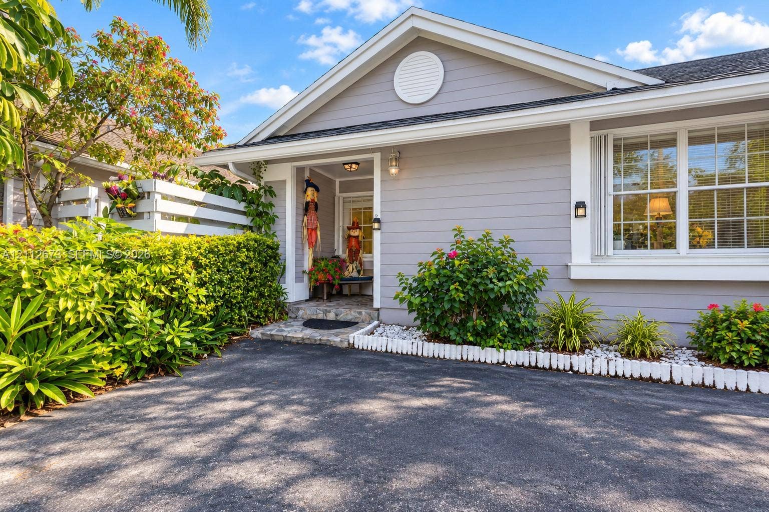 10225 SW 141st Court, #0, Miami, Miami, FL 33186 Single-story residence featuring light gray horizontal siding, a covered entryway with stone-patterned flooring, a gabled roofline, and landscaped exterior beds with white decorative stones