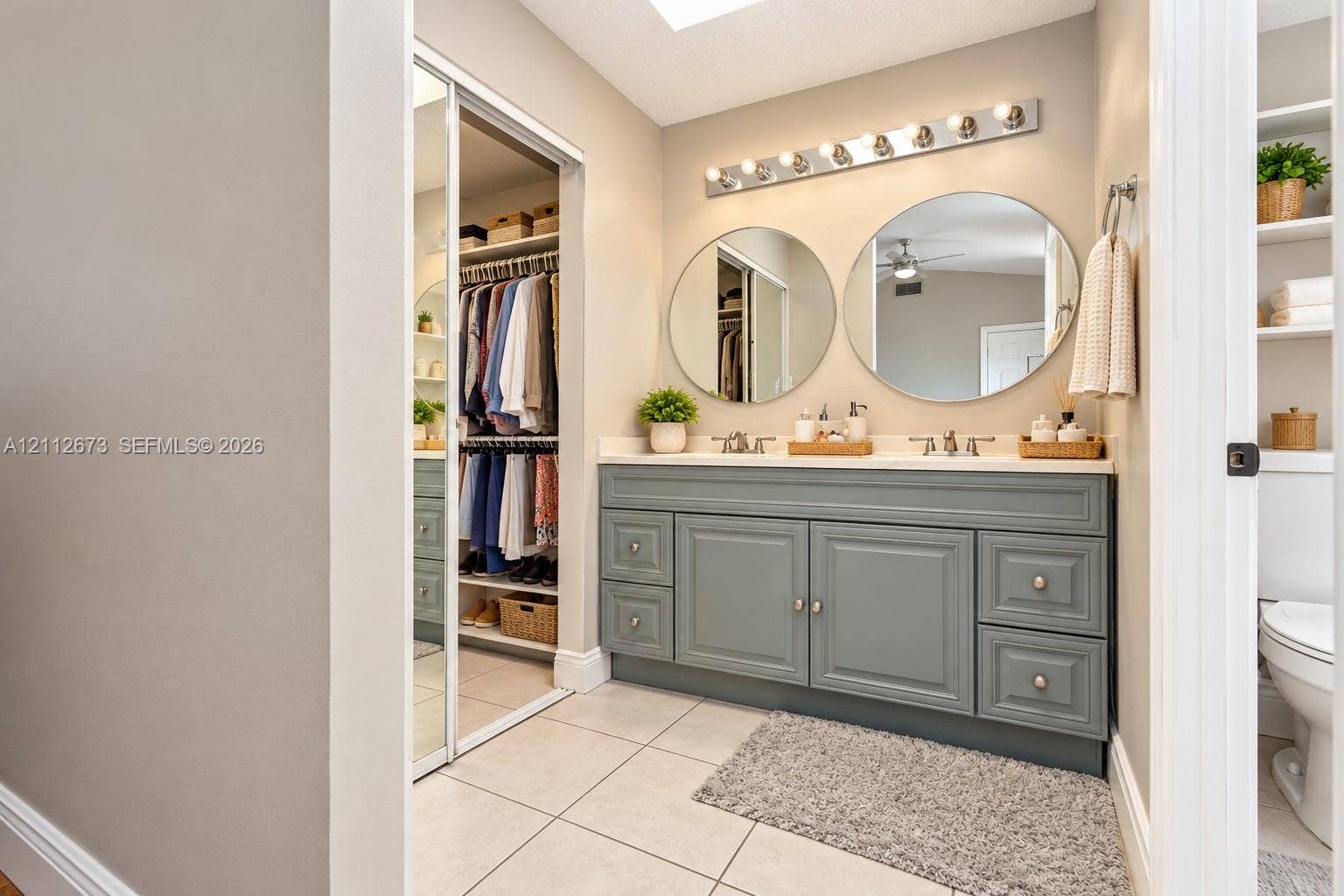 10225 SW 141st Court, #0, Miami, Miami, FL 33186 Bathroom vanity featuring a slate-toned cabinetry base, dual circular wall mirrors, a multi-bulb vanity light fixture, light-toned countertop, and sliding mirrored closet doors