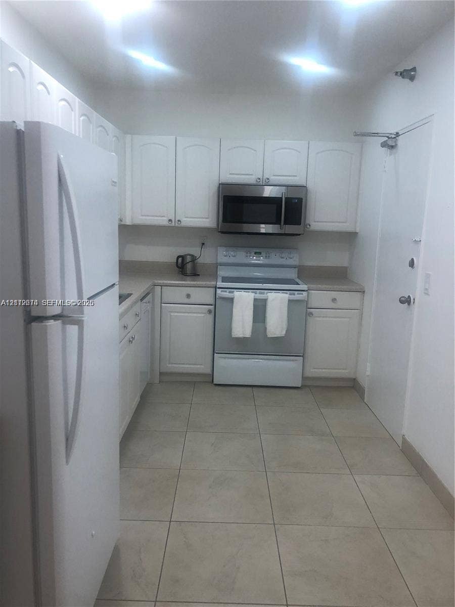 Kitchen featuring white cabinetry, solid-surface countertops, tile flooring, and stainless steel microwave and oven appliances