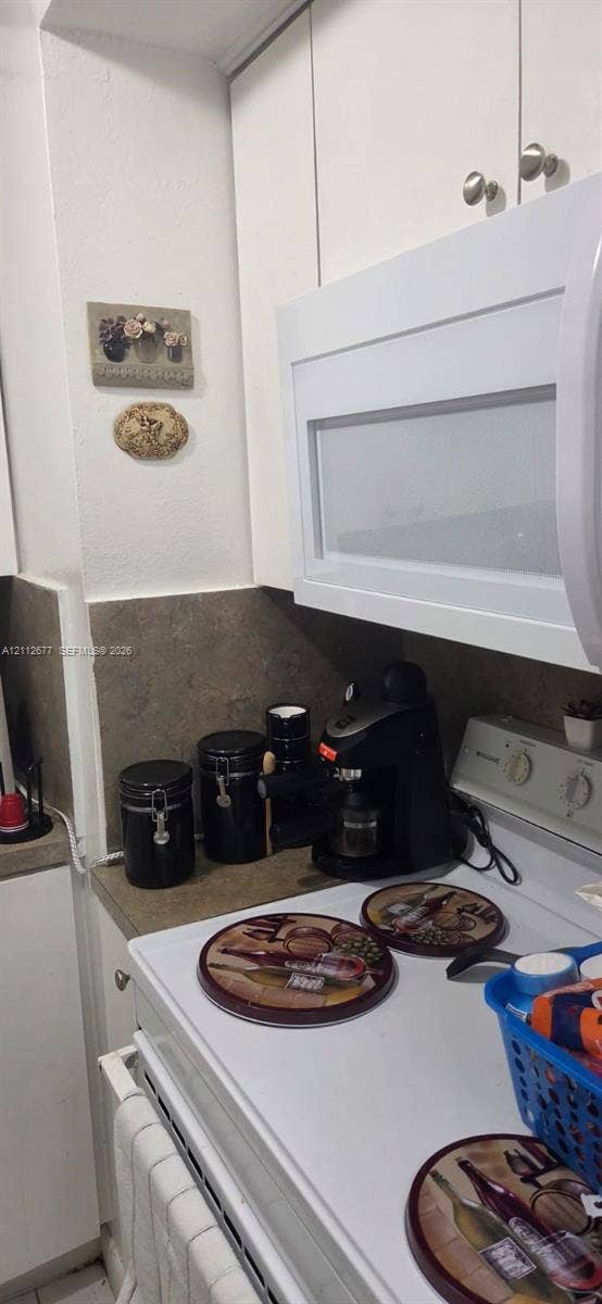 6675 W 4th Avenue, #206, Hialeah, FL 33012 Kitchen featuring white cabinetry, an over-the-range microwave, and neutral-toned backsplash