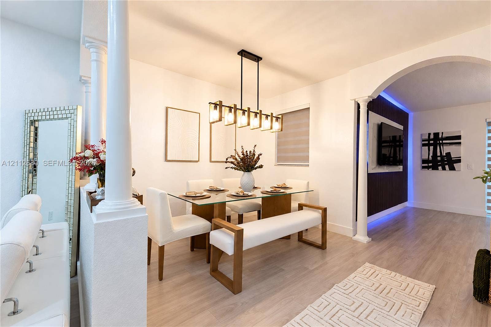 890 SW 154th Path, Miami, FL 33194 Open-concept area featuring decorative columns, arched architectural detail, linear multi-light pendant fixture, wood-finish flooring, and a recessed accent wall with integrated perimeter lighting