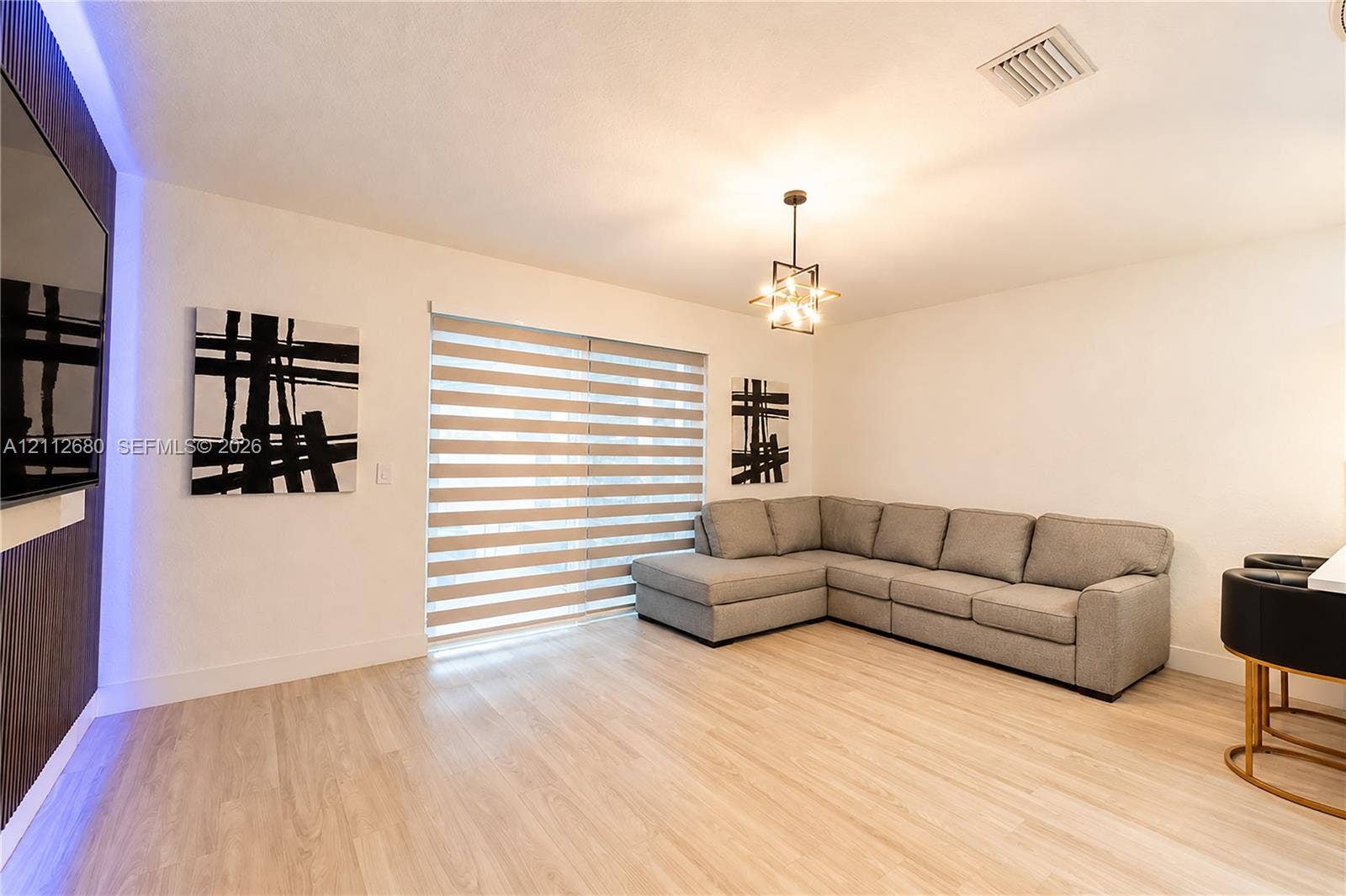 890 SW 154th Path, Miami, FL 33194 Living area featuring wood-finish flooring, a contemporary multi-light pendant fixture, integrated blue accent lighting, and dual-layered window shades
