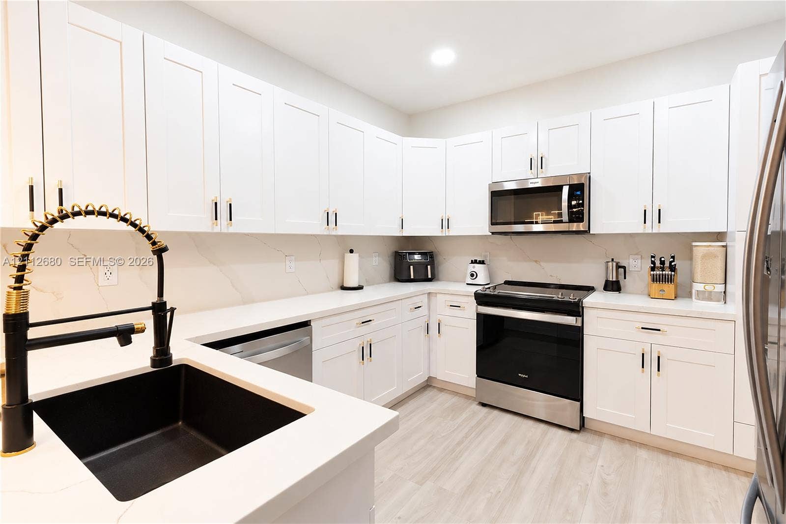 890 SW 154th Path, Miami, FL 33194 Kitchen featuring white shaker-style cabinetry, white countertops with subtle veining, undermount sink with a matte black pull-down faucet, stainless steel appliances, and wood-finish flooring
