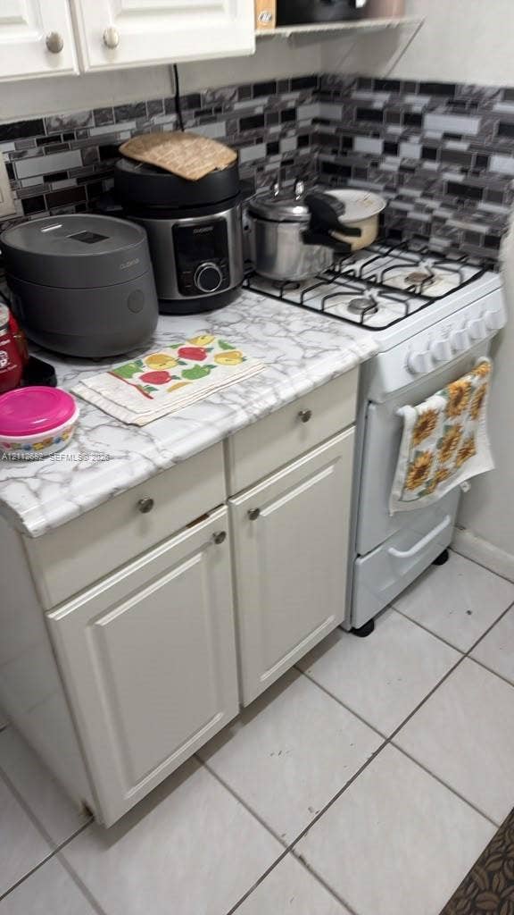 1655 W 44th Place, #435, Hialeah, FL 33012 Kitchen featuring white shaker-style cabinetry, a stone-pattern laminate countertop, a four-burner gas range, a multi-tonal glass tile backsplash, and tile flooring