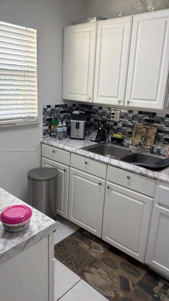 1655 W 44th Place, #435, Hialeah, FL 33012 Kitchen area featuring white cabinetry, stone-patterned laminate countertops, double-basin stainless steel sink, and a decorative mosaic tile backsplash