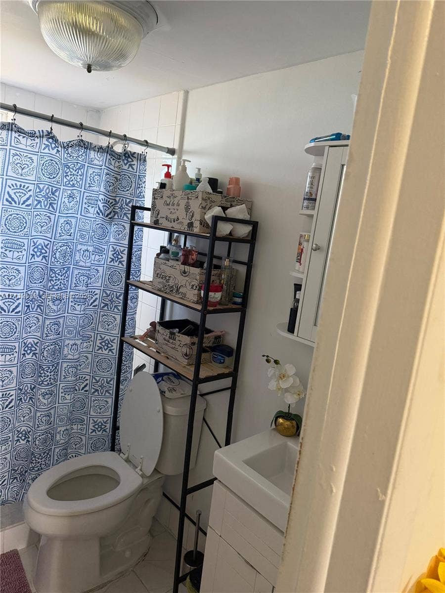1655 W 44th Place, #435, Hialeah, FL 33012 Bathroom featuring a white vanity cabinet, ceramic sink, wall-mounted white storage shelving, and a flush-mount dome light fixture