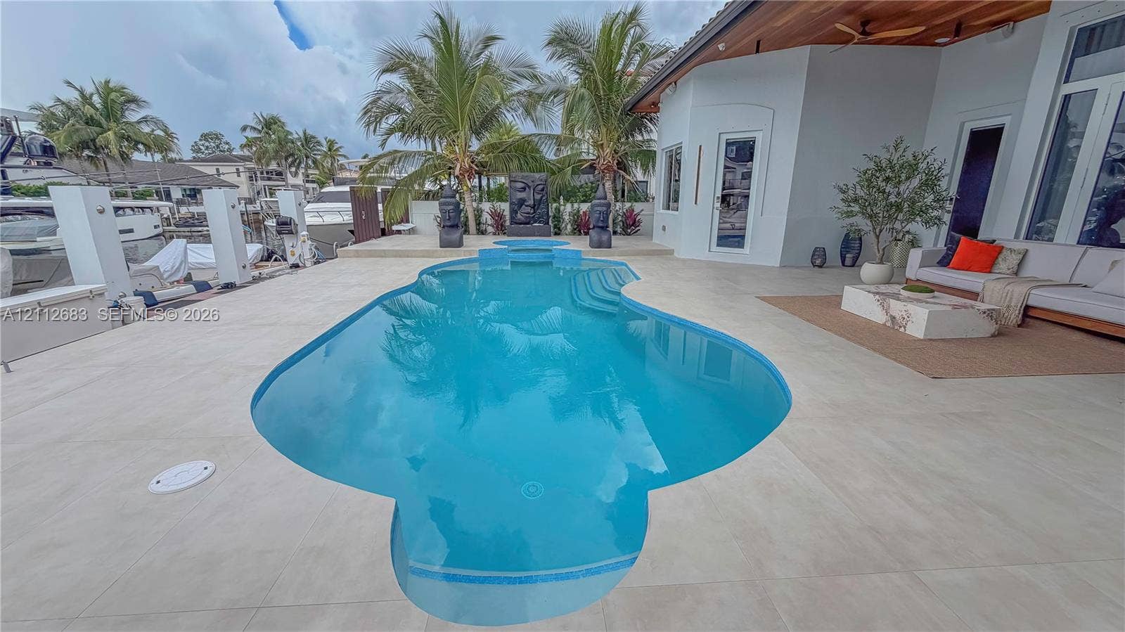 Custom swimming pool with integrated sun shelf and tiled coping, oversized light-toned stone pool deck, wood-planked covered patio ceiling, and private deep-water dock