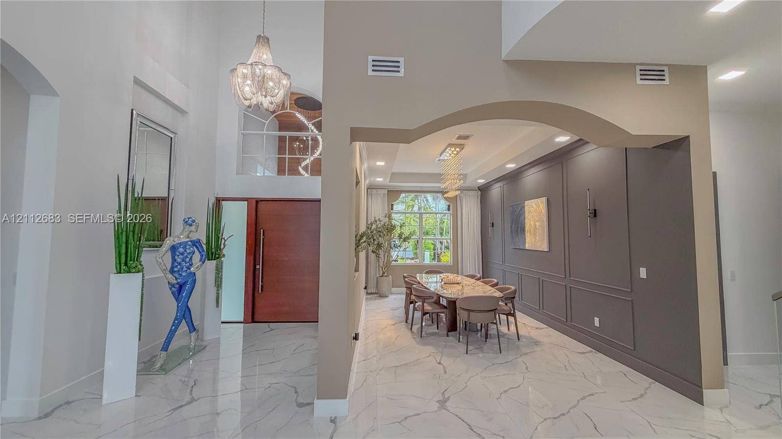 Grand foyer featuring high ceilings, stone-finish flooring, a contemporary chandelier, and an arched entryway leading to a formal area with decorative wall molding