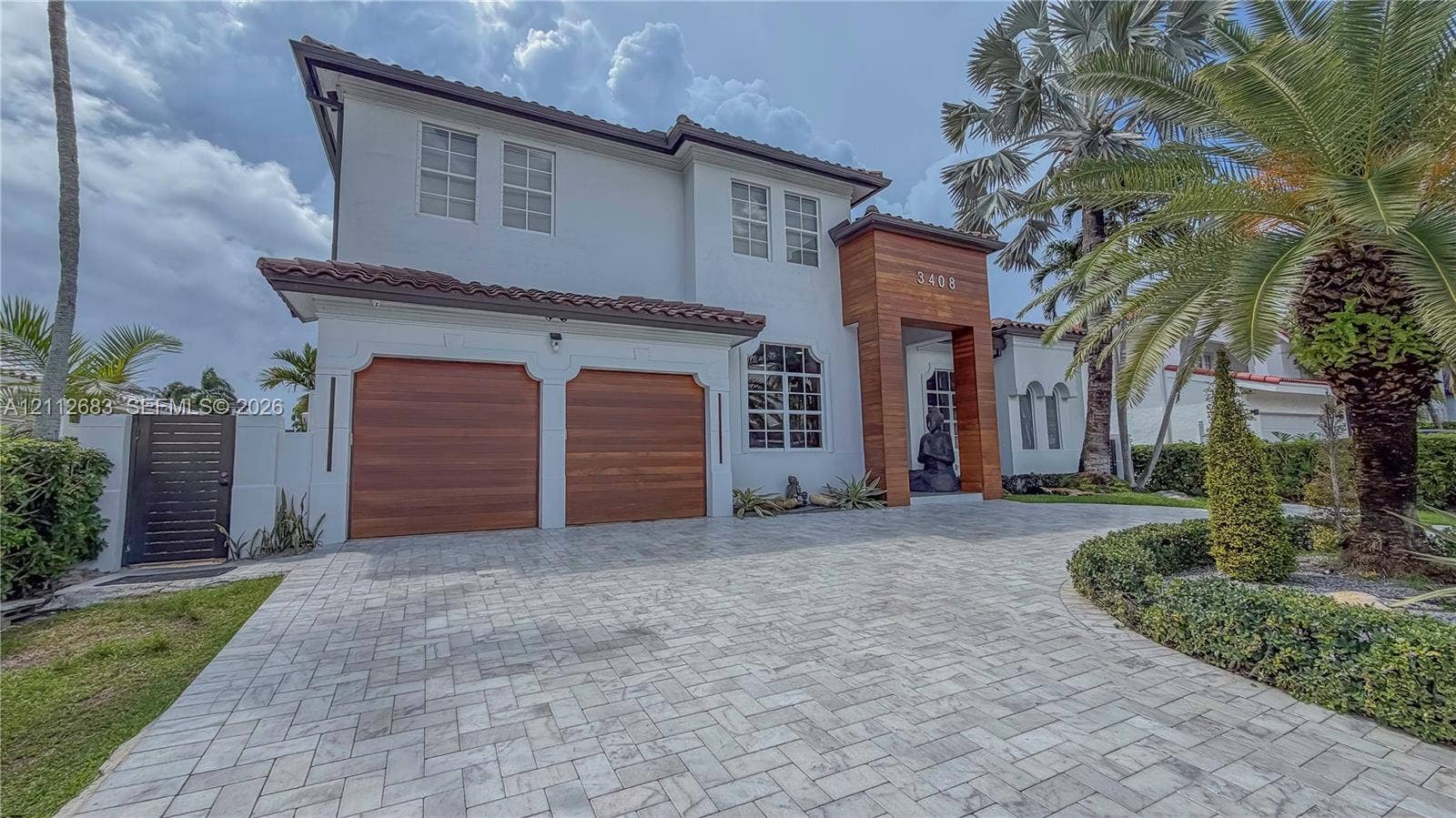 Two-story exterior featuring a stone-paver driveway, dual wood-finish garage doors, wood-paneled entryway accent, and a clay tile roof