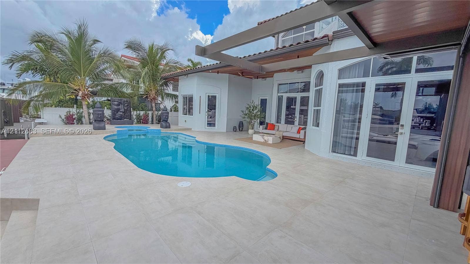 Outdoor patio featuring large-format tile flooring, a custom swimming pool with built-in spillway, a covered pergola structure, and expansive glass paneled doors