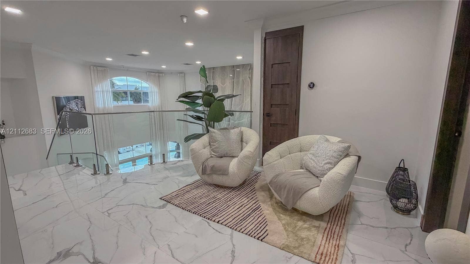 Polished stone-finish flooring with veining, glass panel railing with stainless steel standoffs, recessed ceiling lighting, and a dark wood-finish five-panel interior door