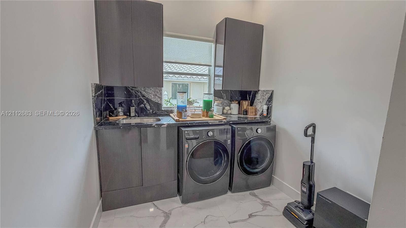 Dark wood-finish cabinetry, stone-look backsplash, built-in stainless steel sink, and large-format tile flooring