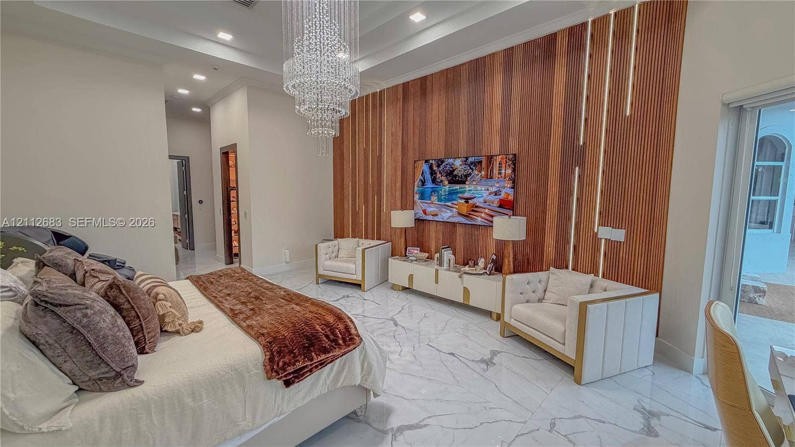 Tray ceiling with recessed lighting, large crystal chandelier, polished stone flooring, and vertical wood-slat accent wall with integrated LED strip lighting