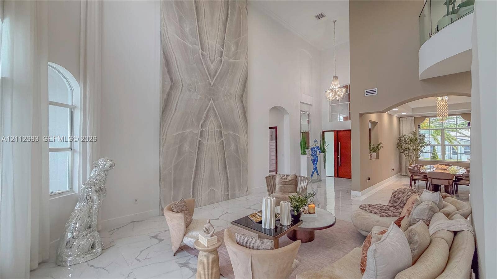 Double-height ceiling, floor-to-ceiling stone-cladding feature wall, polished stone flooring, glass-railing gallery, and tiered crystal chandelier