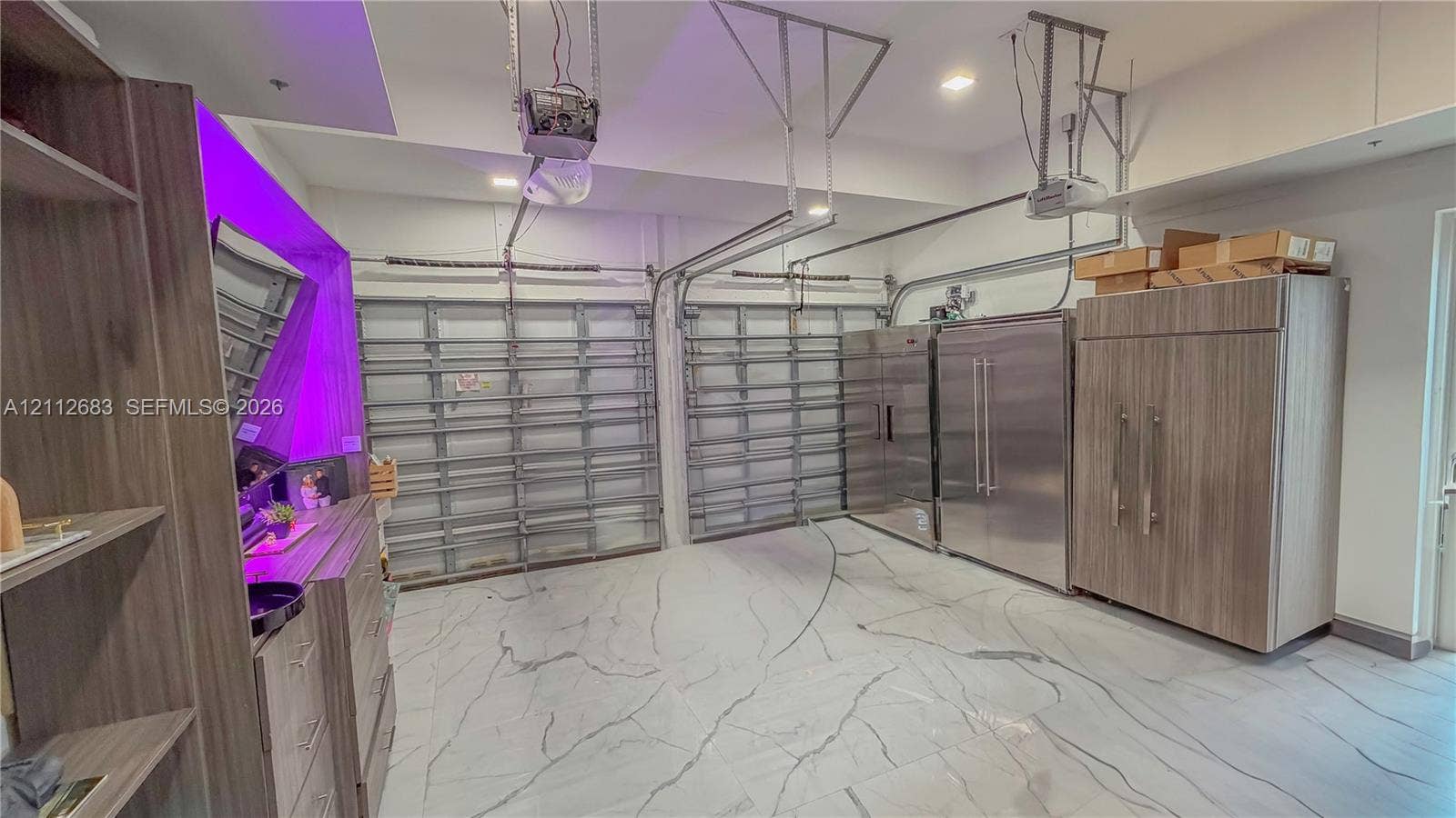 Multi-car garage featuring large-format tile flooring, integrated stainless steel refrigeration units, and custom wood-finish cabinetry
