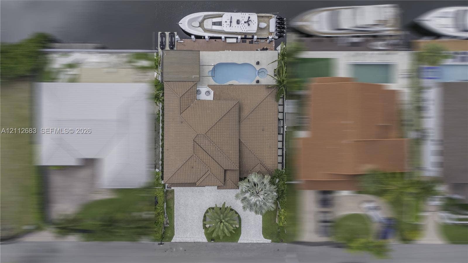 Aerial perspective featuring a tile roof, private swimming pool with integrated spa, paved driveway, and deep-water dockage