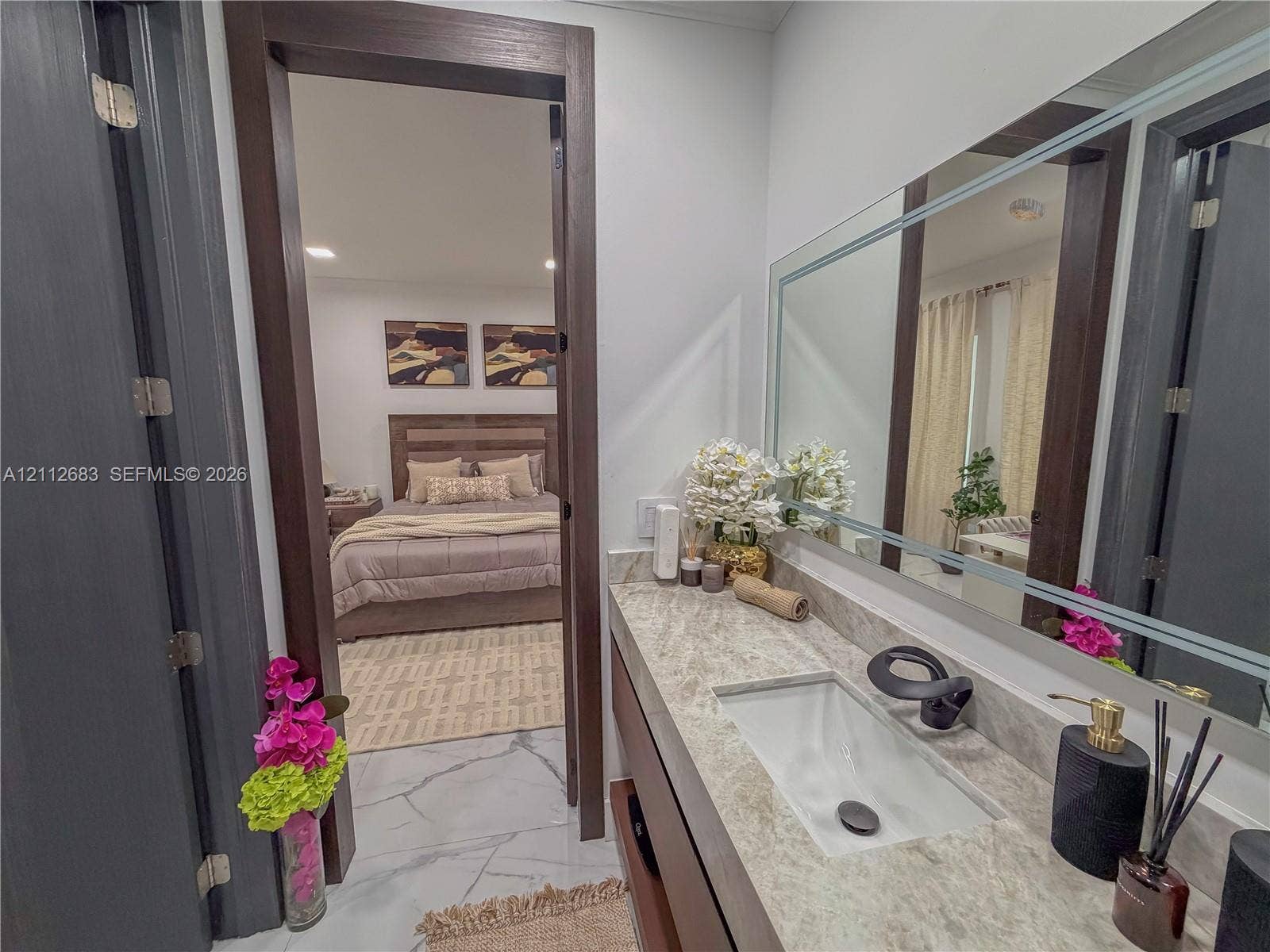 Vanity featuring a rectangular undermount sink, stone countertop, matte black faucet, and a large framed mirror with integrated lighting
