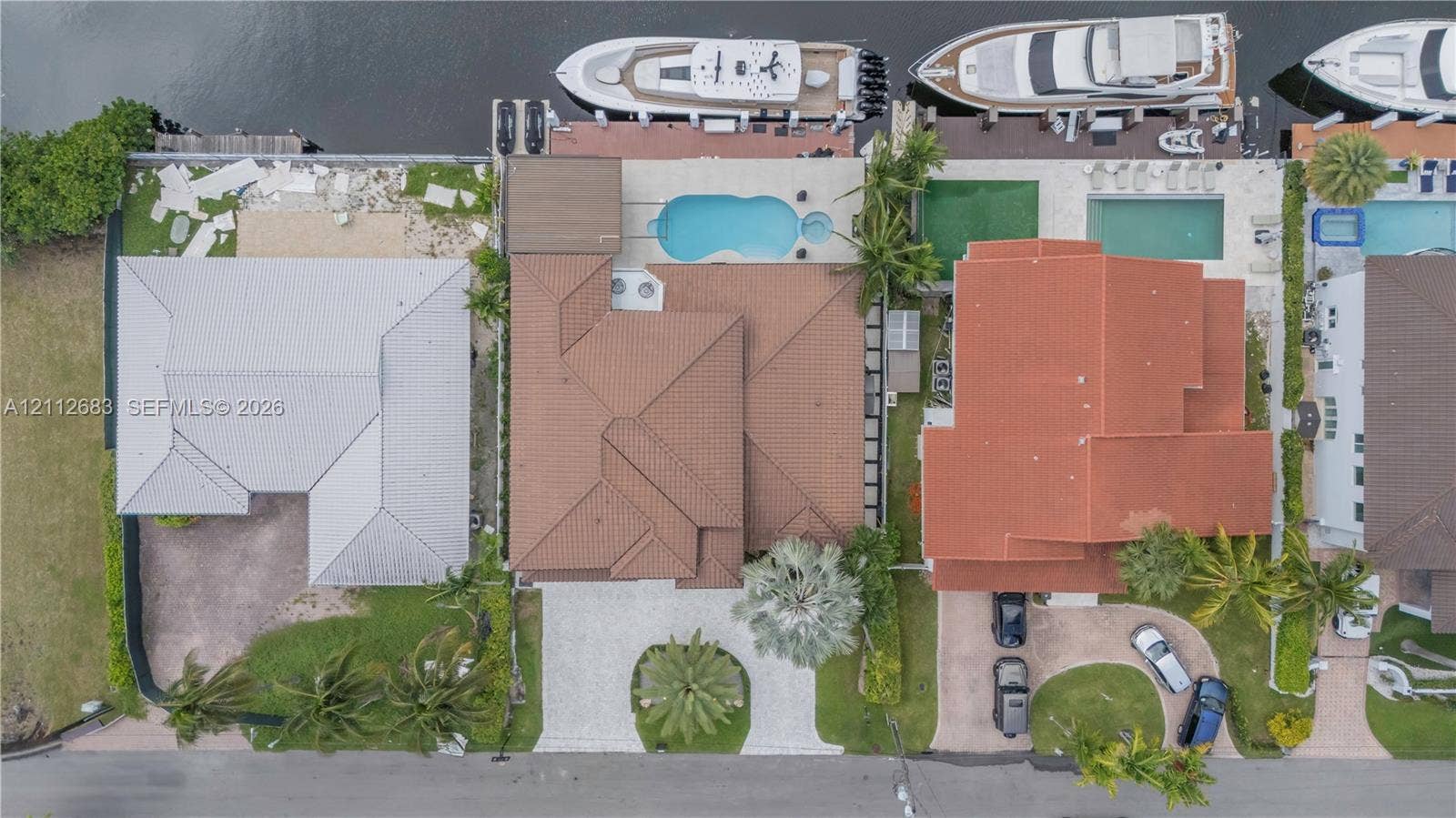 Aerial perspective featuring a tile roof, paved circular driveway, rear swimming pool with integrated spa, and deep-water canal bulkhead