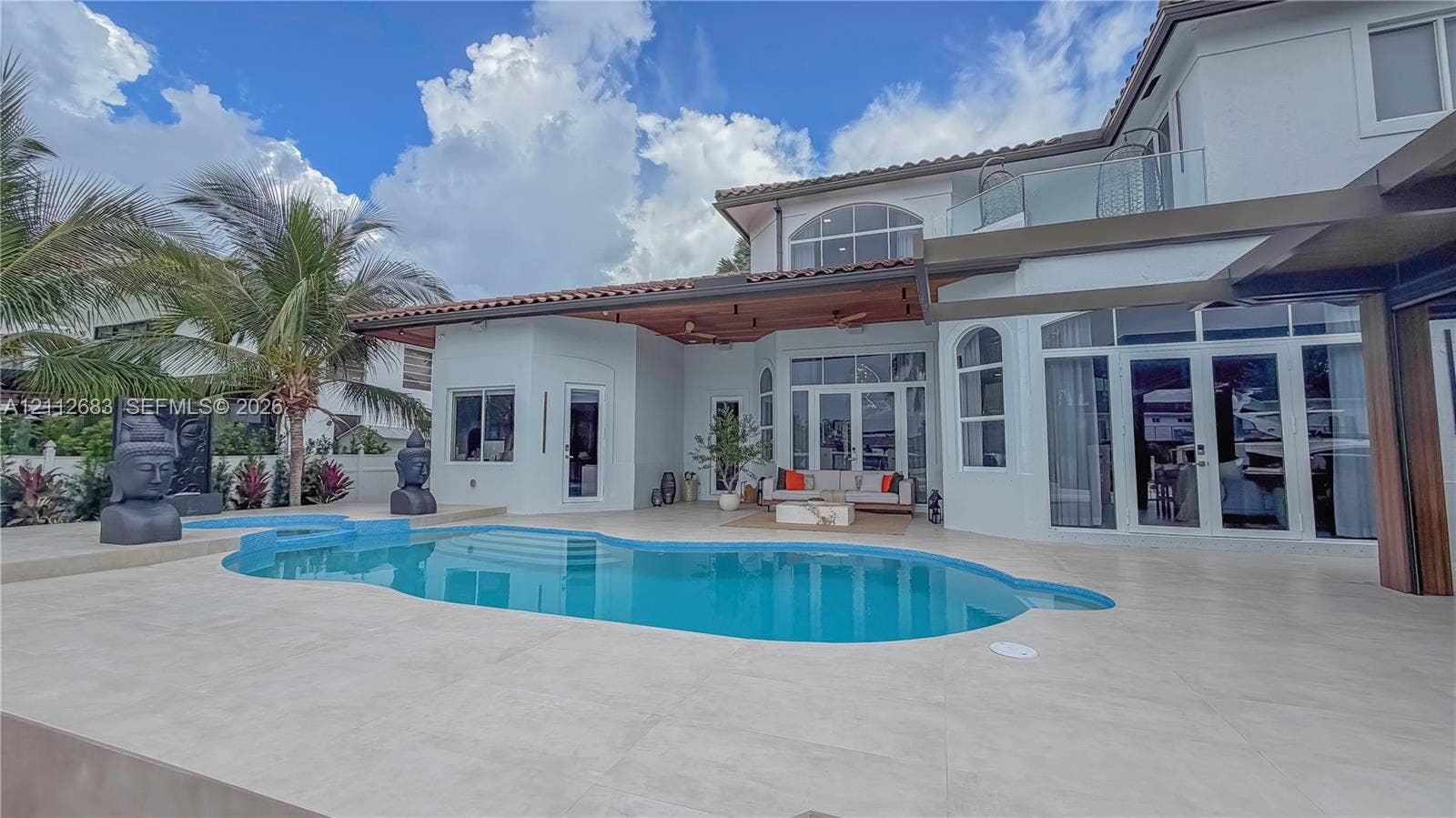 Rear exterior featuring a covered patio with recessed lighting, an inground swimming pool with integrated spa, large-format tile decking, and an upper-level glass-railed balcony