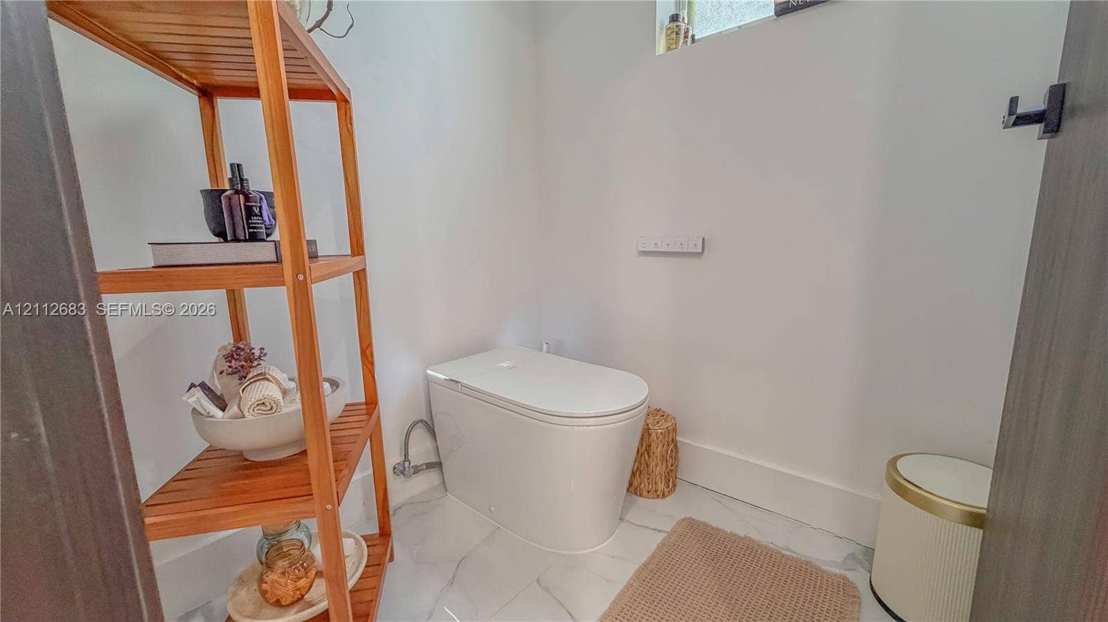Contemporary one-piece toilet featuring a smooth, minimalist profile and high-gloss white finish, complemented by polished stone-finish flooring with distinct veining
