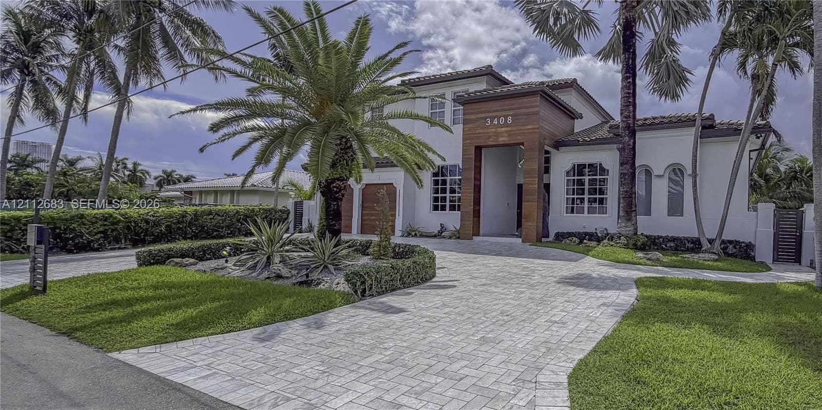 Two-story exterior featuring white stucco finish, wood-plank architectural accents, paver driveway, arched windows, and manicured landscaping