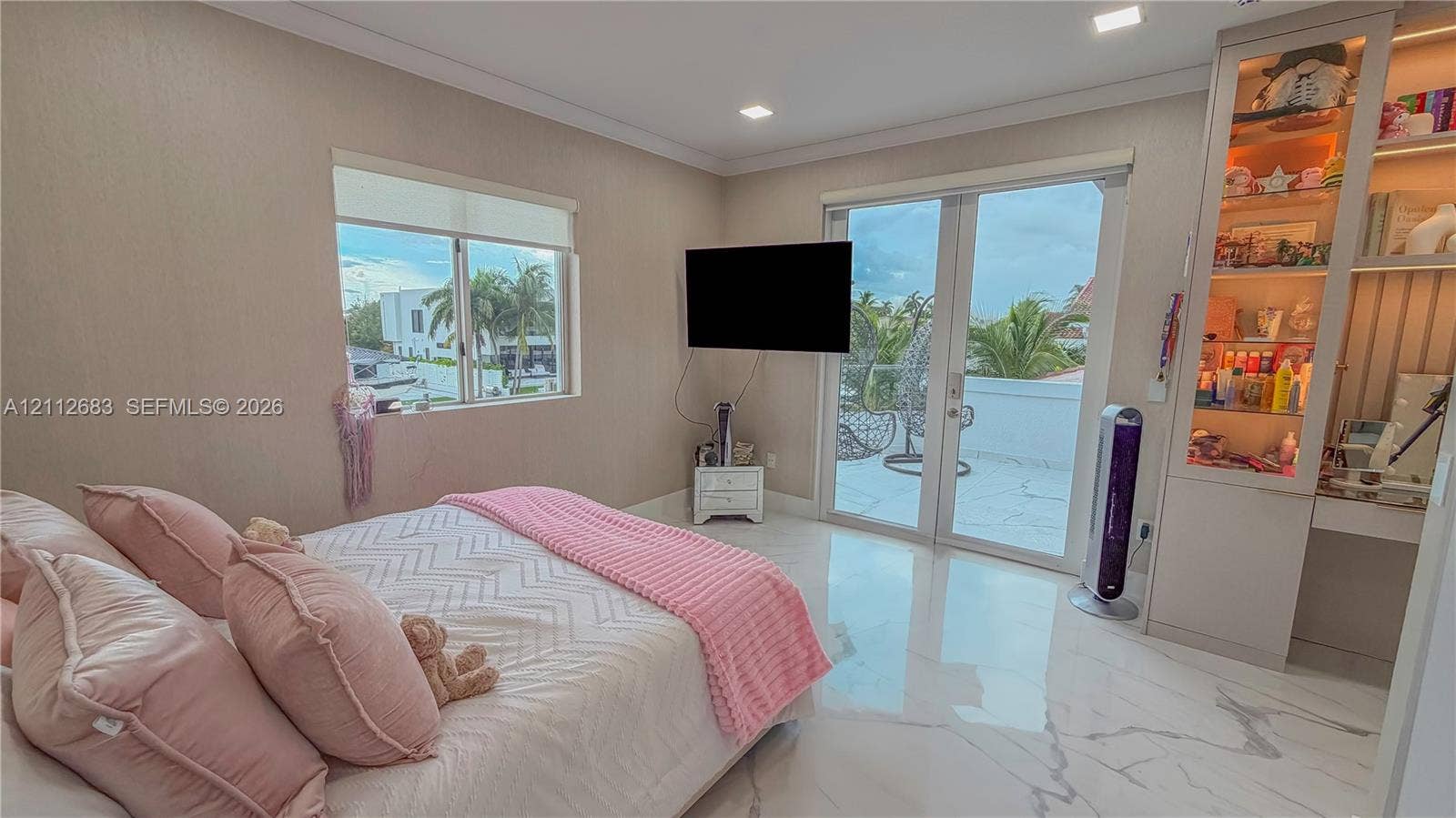 Neutral-toned room featuring large-format tile flooring, recessed lighting, built-in floor-to-ceiling cabinetry with integrated display lighting, and glass-paneled double doors providing access to a balcony