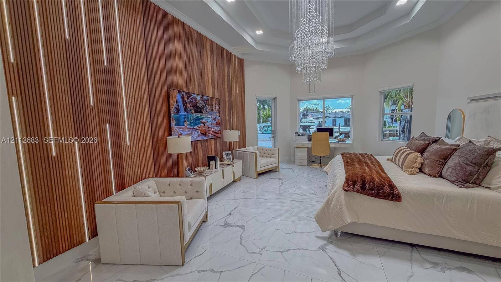 Accent wall with floor-to-ceiling wood slats and integrated linear lighting, large-format tile flooring, multi-tiered crystal chandelier, and tray ceiling
